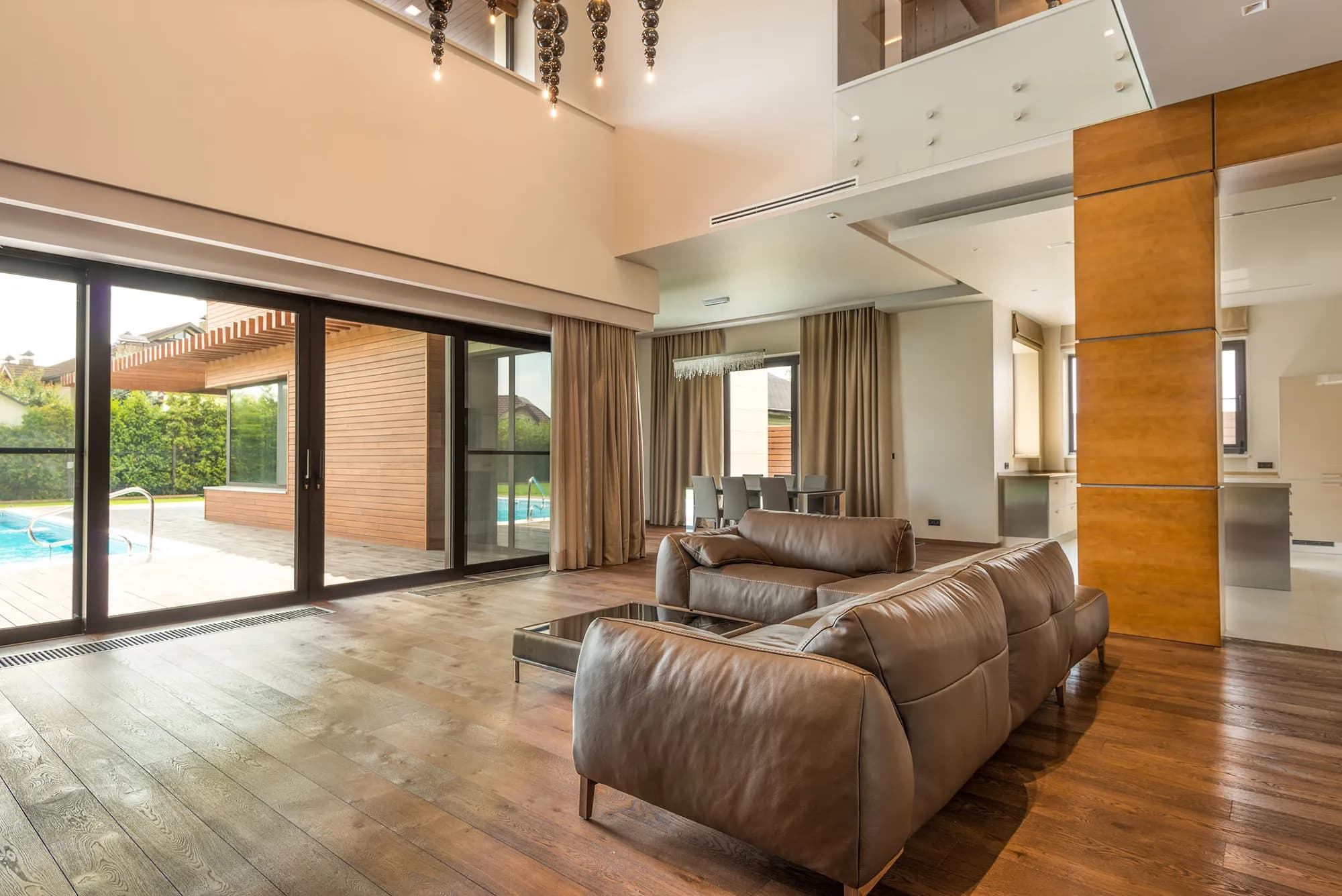 Modern living room with large windows, comfortable seating, and an open view of a pool outside.